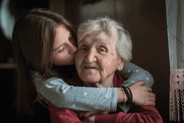 Young girl hugs and kisses her elderly grandmother, capturing the deep bond that reminds us grandkids need our stories.